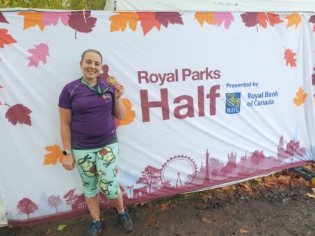 Me in running kit standing in front of Royal Parks Half branding with medal