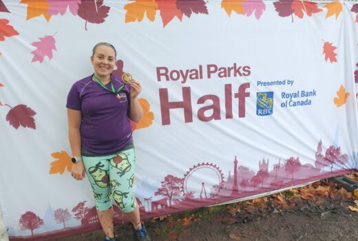 Me in running kit standing in front of Royal Parks Half branding with medal