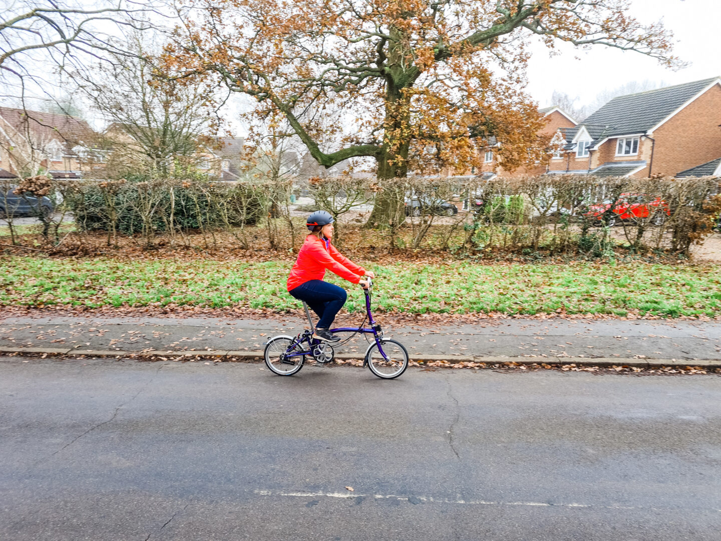 Woman in pink cycling jacket and helmet riding a Brompton bike along the road