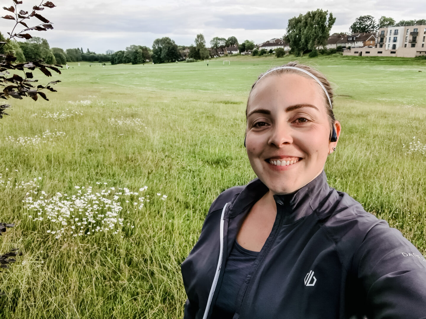 Selfie of woman wearing grey running kit with a green field behind her
