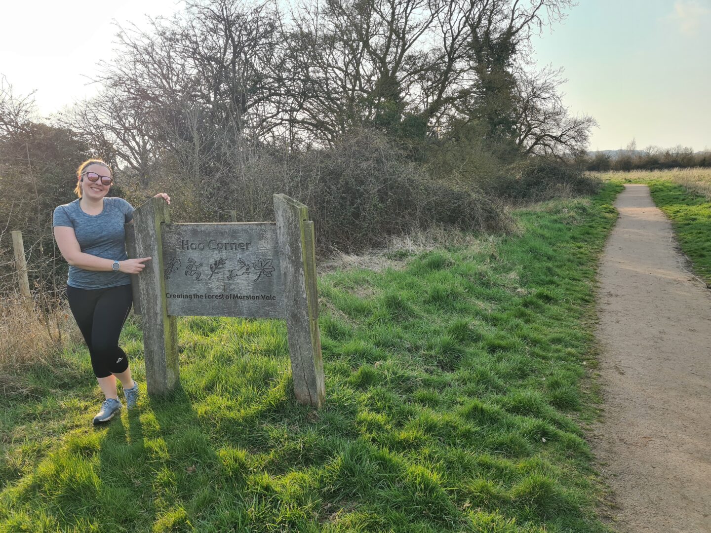 Woman in running kit standing next to a sign that says Hoo Corner on a running trail