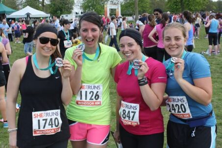 four women smile at the camera holding up their race medals