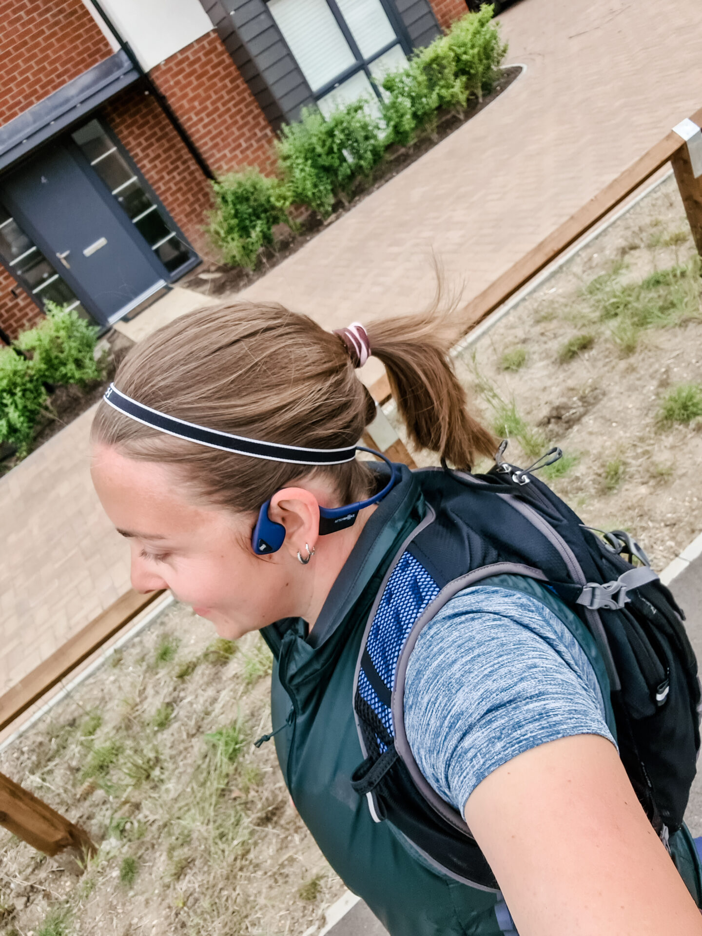 Side profile of a woman running with a backpack, and green gilet