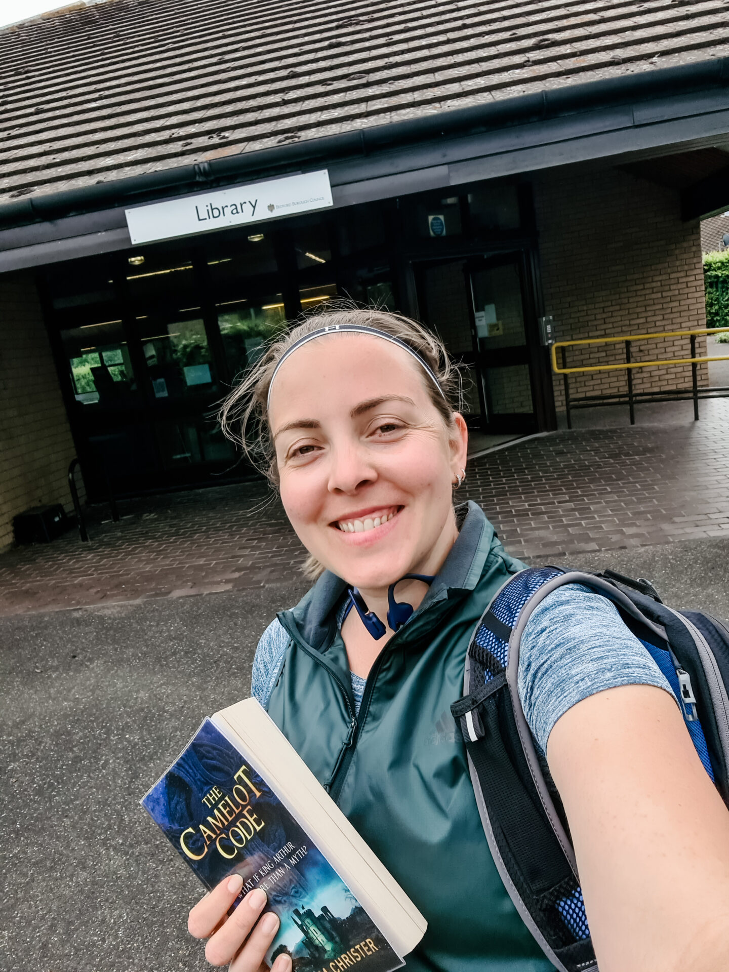 Smiling face of a woman in running kit standing in front of a building that says library