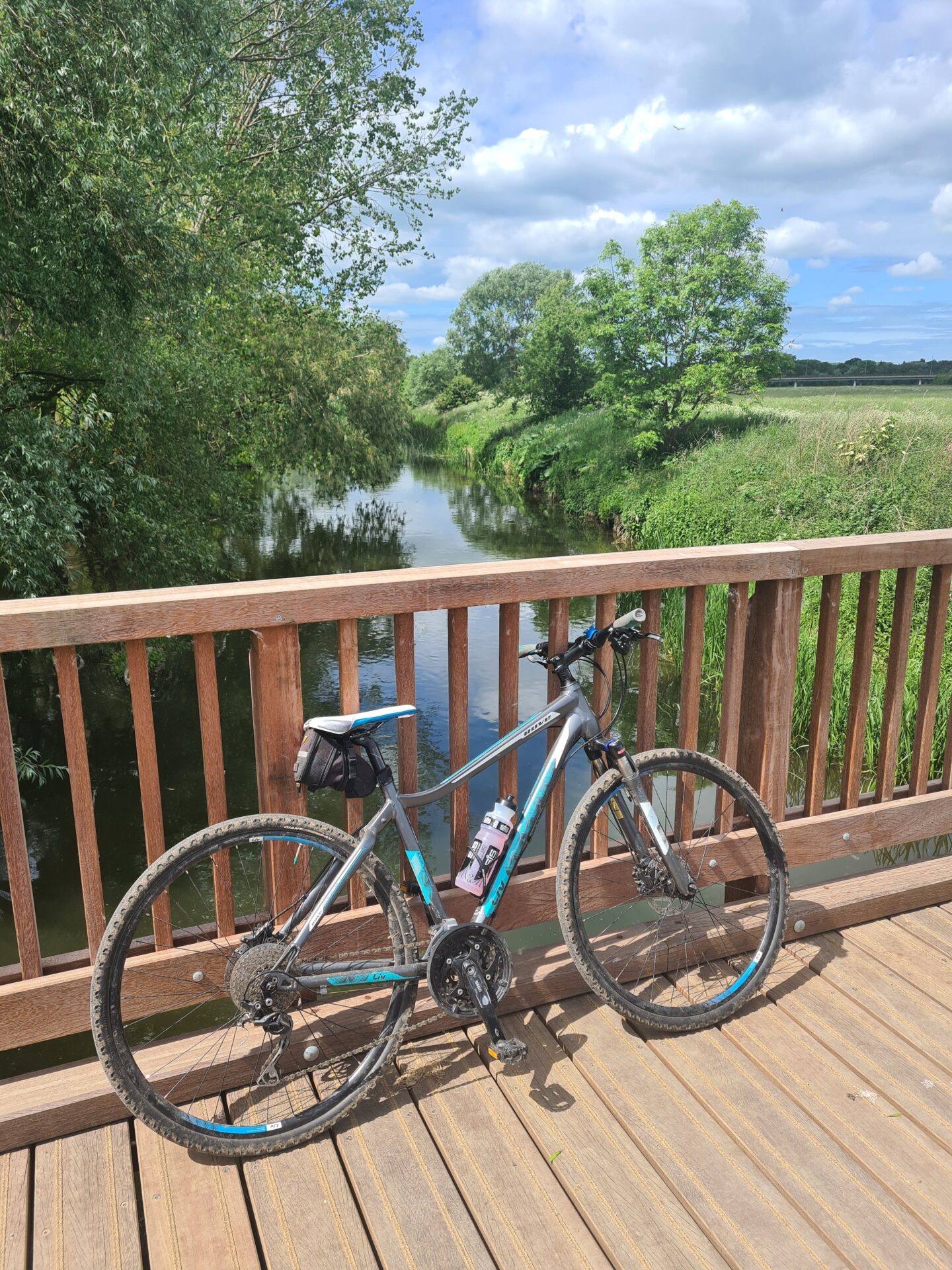 image of a blue and grey bike leaning on the wooden railings of a bridge over a river