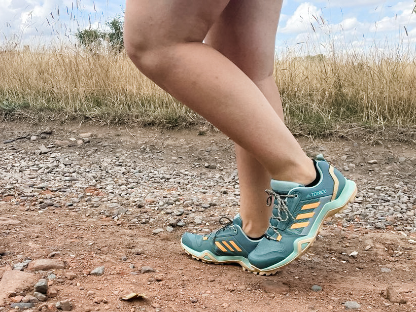 Image of legs wearing green and orange adidas hiking shoes, walking on a dusty trail