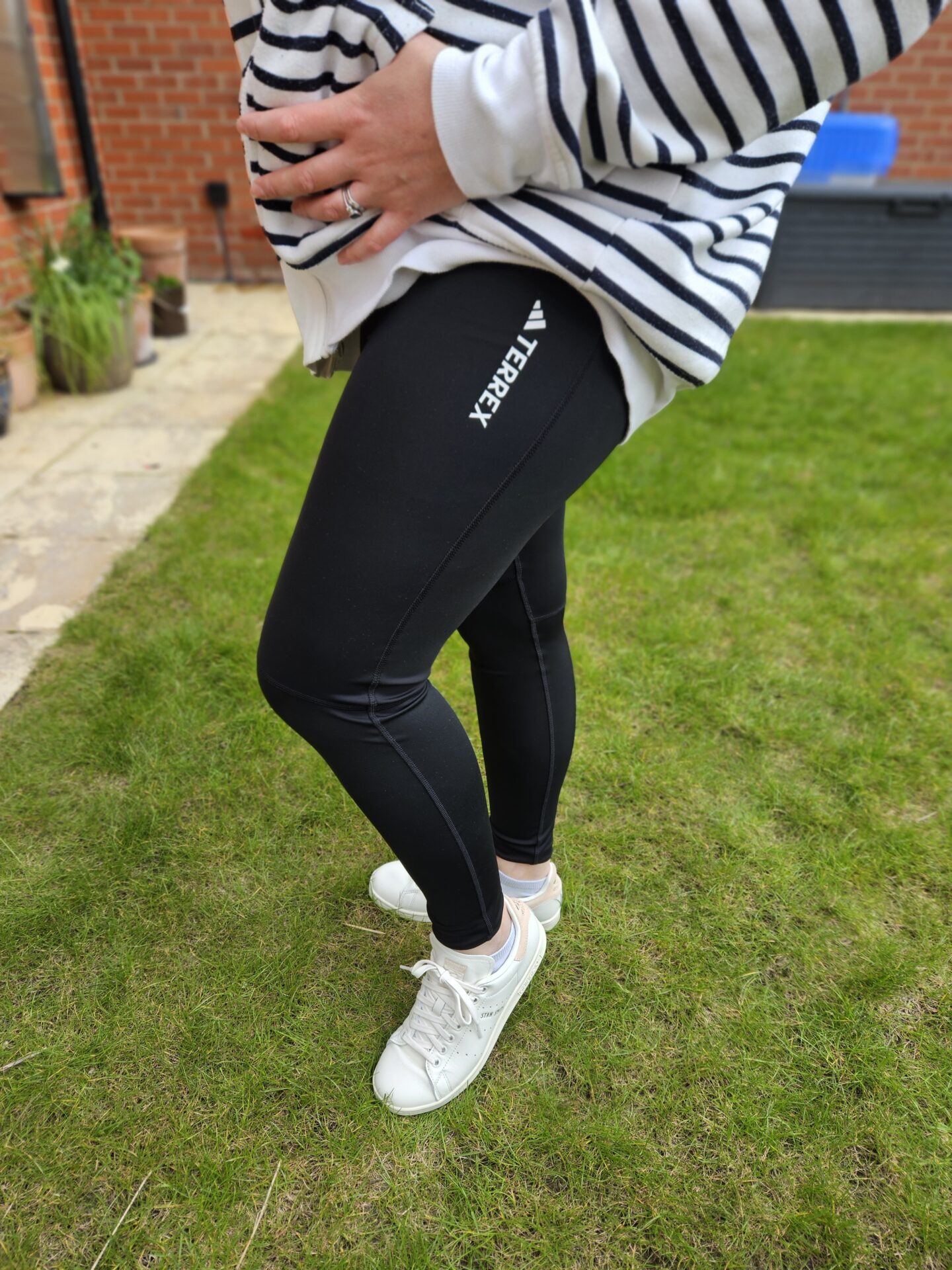 Woman's legs wearing black leggings, white trainers and a blue and white striped hoody. She is standing on green grass. 