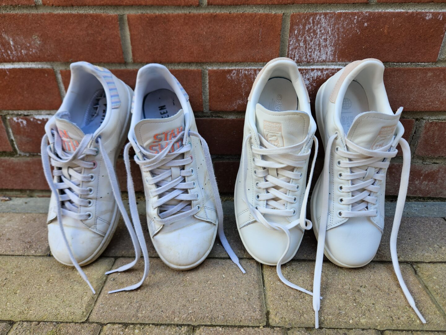 Two pairs of white trainers leaning up against a red brick wall. The pair of trainers on the left are old and worn, the pair on the right are brand new and pristine white.