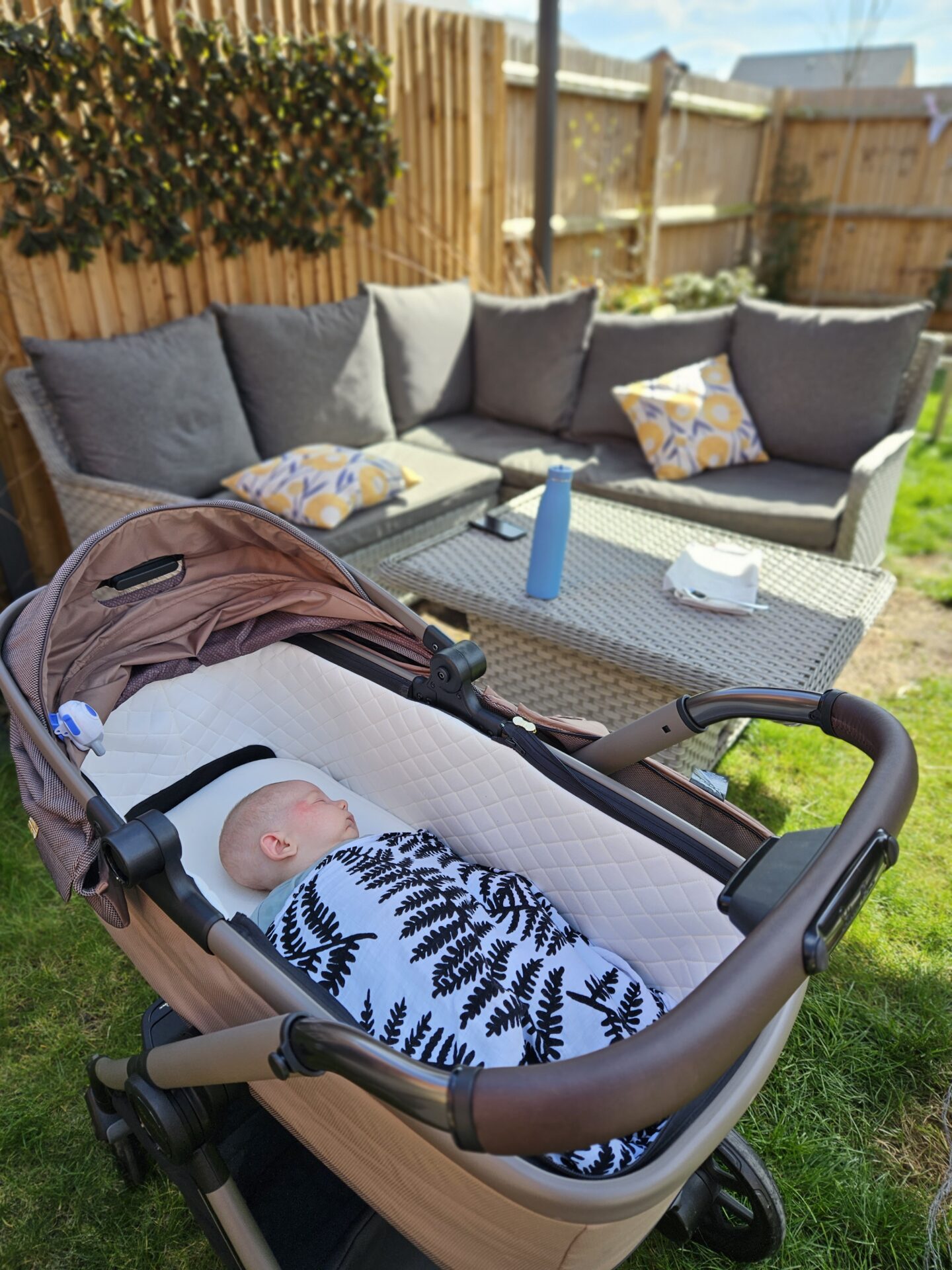 baby sleeping in a pram in a garden with garden furniture in the background