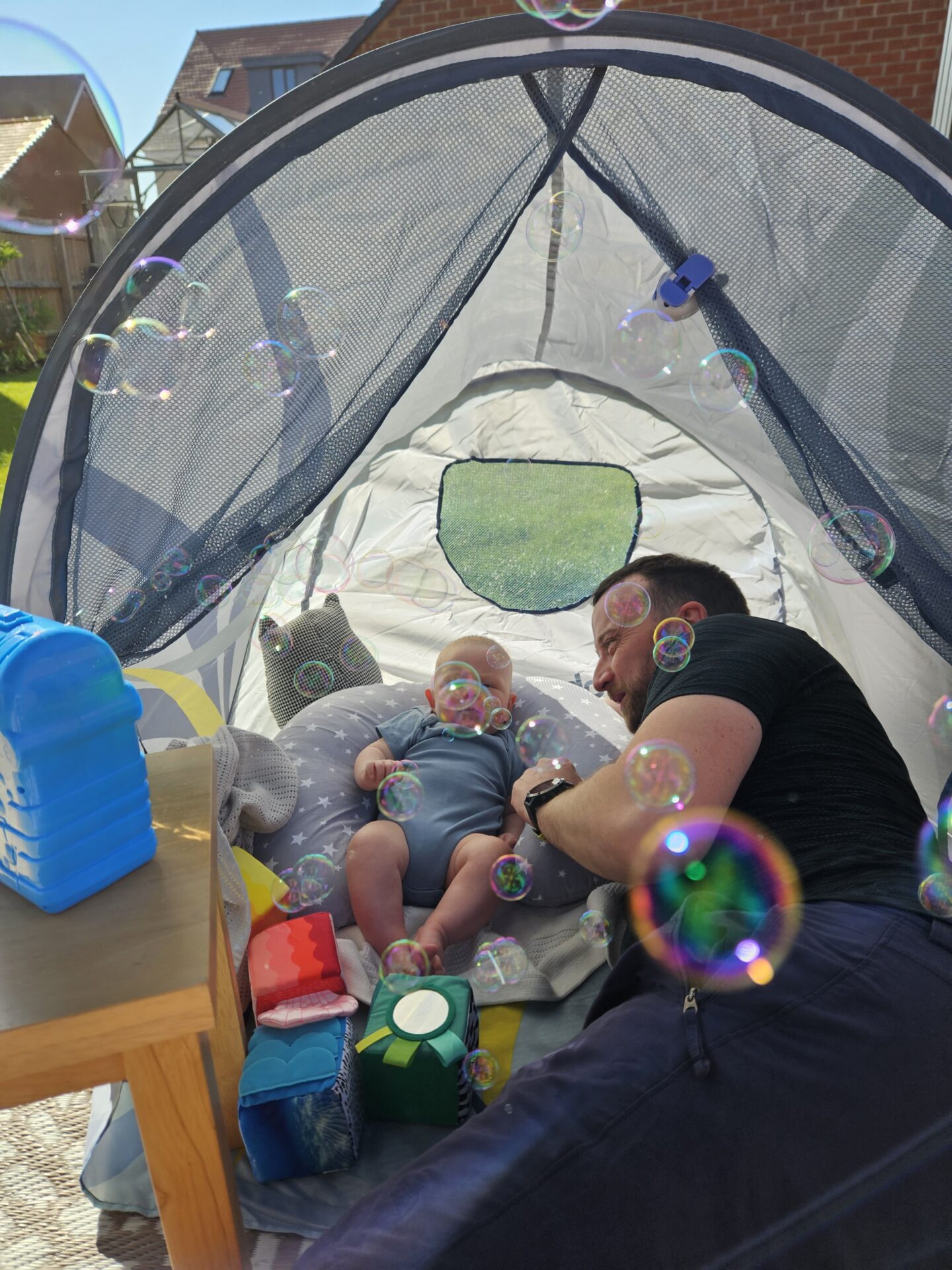 man and baby sitting inside a play tent with bubbles from a bubble machine blurring their faces 