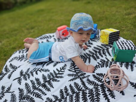 Baby in an adidas outfit is lying on a black and white playmat with toys around him