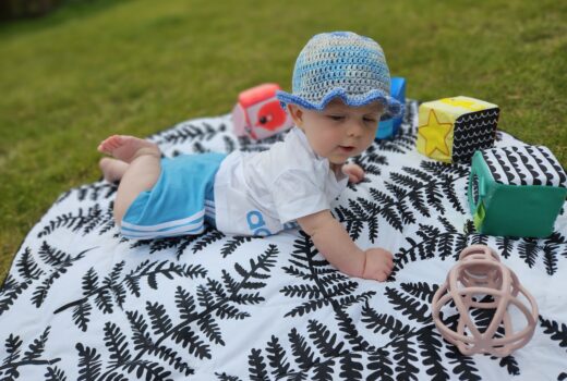 Baby in an adidas outfit is lying on a black and white playmat with toys around him