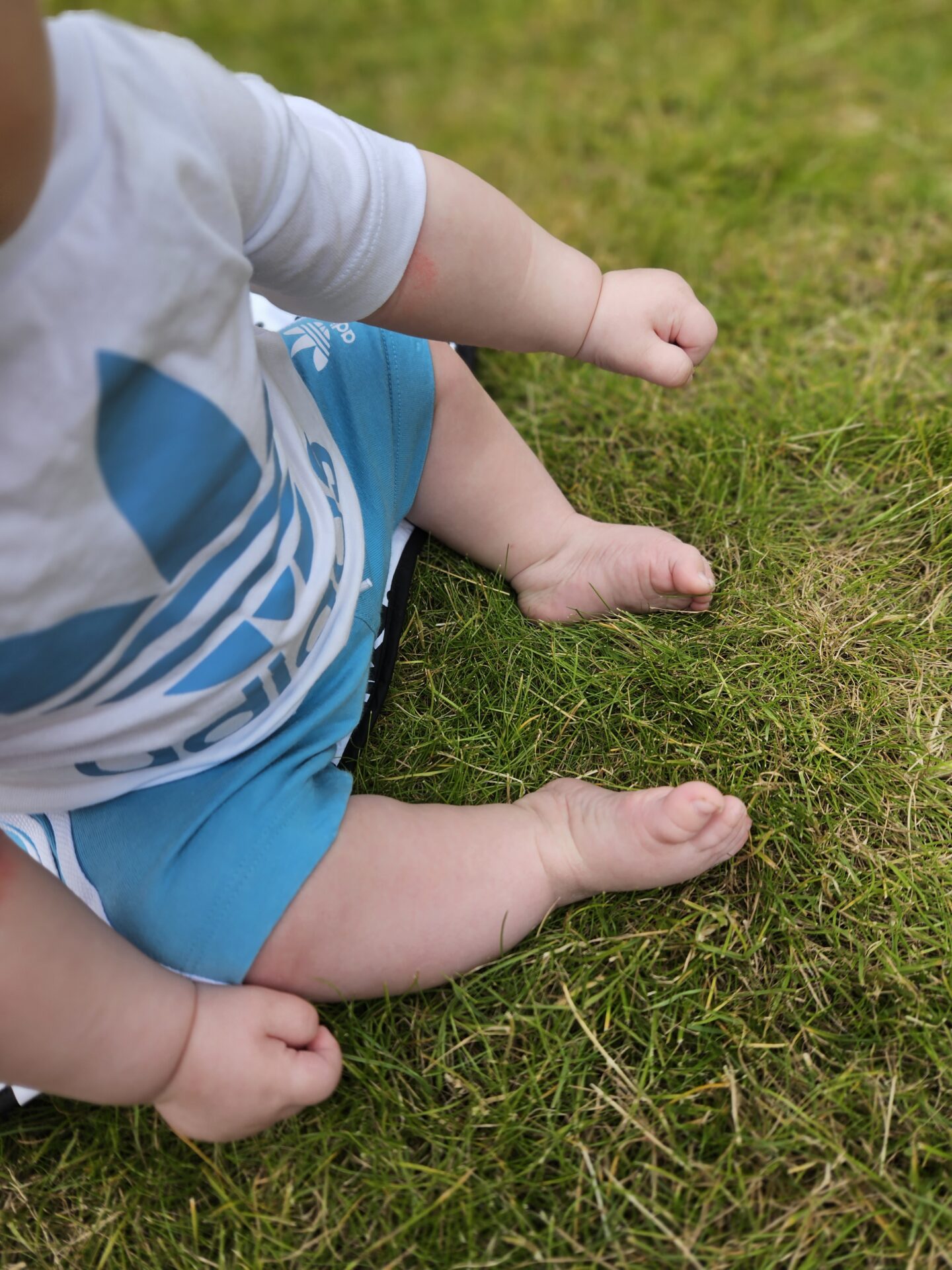 baby sitting on the green grass, just his toes and lower body are visible