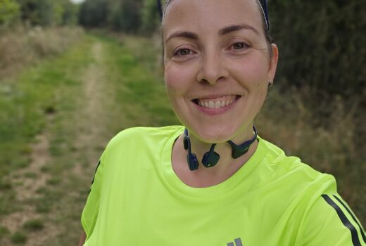 woman in yellow running top smiles at the camera, with a green grassy trail behind her