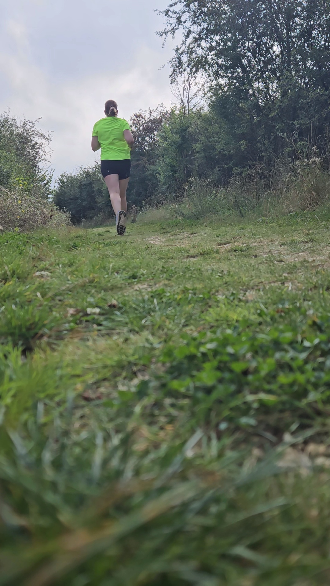 grassy running trail with woman in black shorts and yellow top running away into the distance