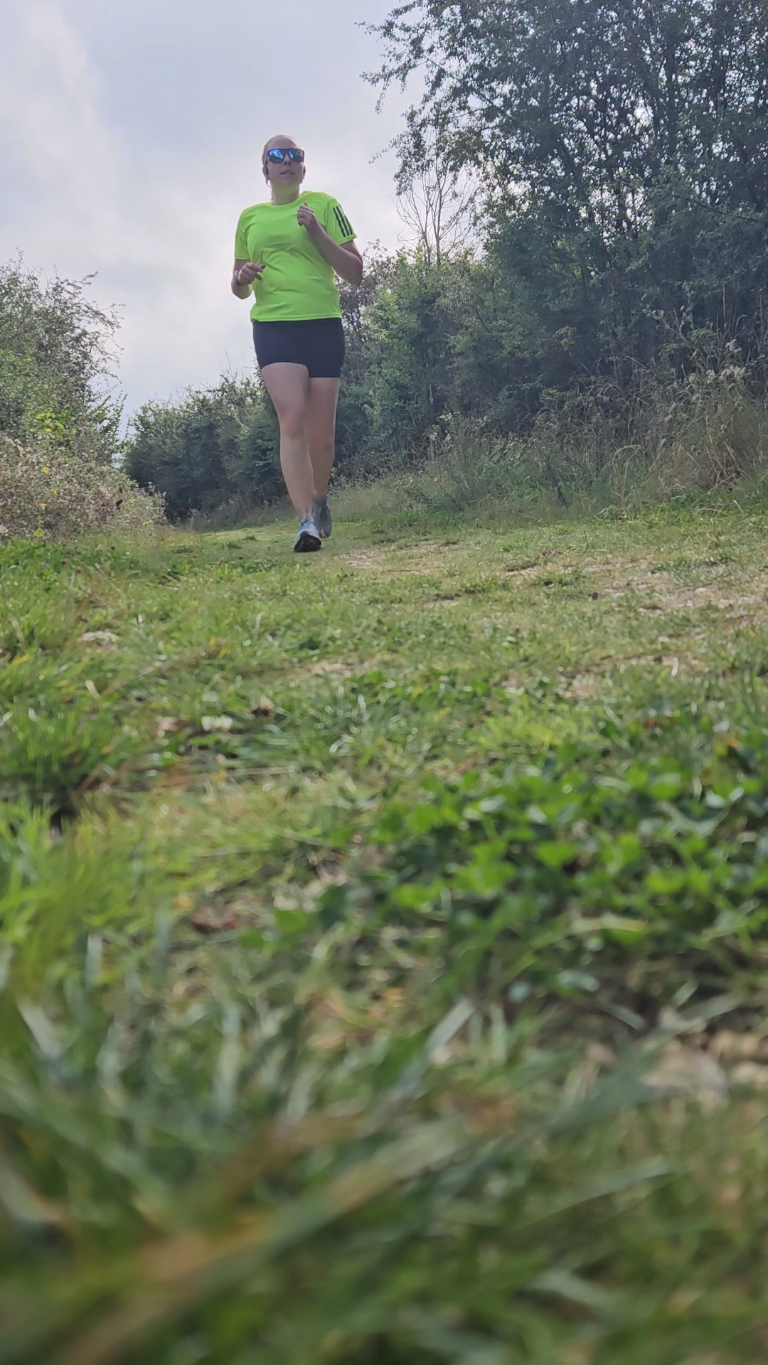 grassy running trail with woman in black shorts and yellow top running towards the camera