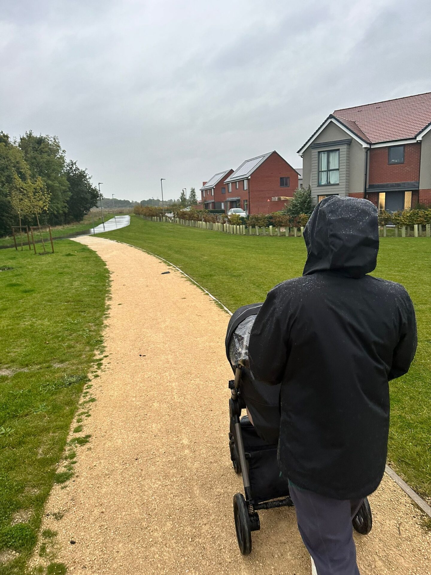 Back of a person in black waterproof coat pushing a pushchair in the rain