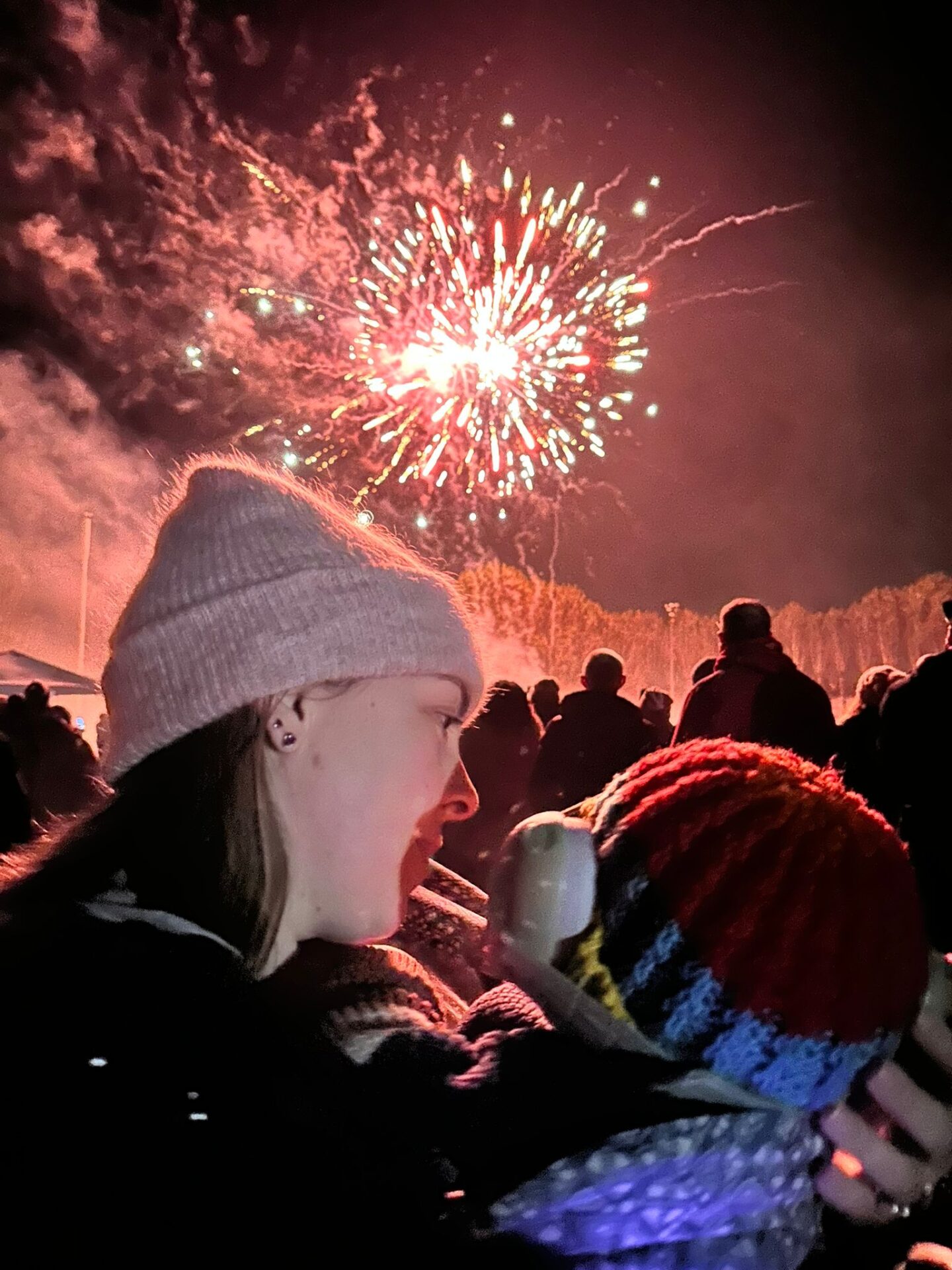Back of a baby's head as he gazes up at the sky at fireworks. Woman carrying baby looks into his face. 