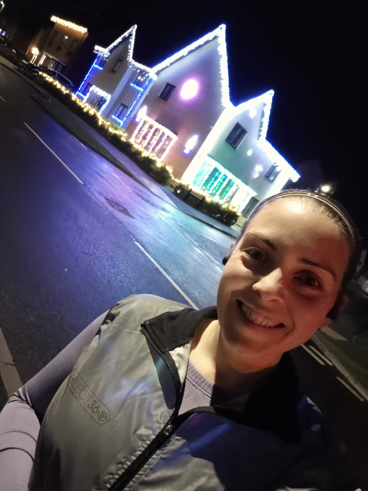 Selfie of a woman in running kit with a house lit up by colour Christmas lights behind her.