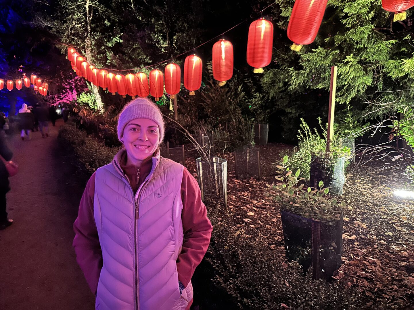 Woman in fleece and gilet and beanie hat standing in front of a row of red Chinese lanterns at night